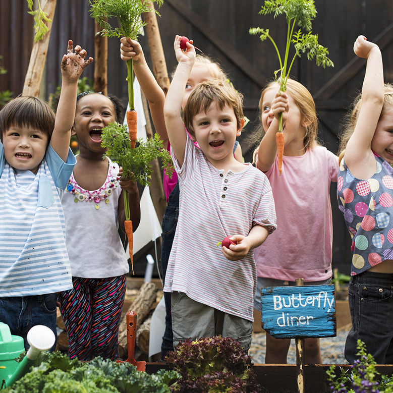 Children holding carrot in a garden