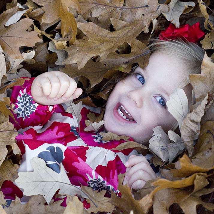 cute little girl is buried and surrounded by Fall leaves